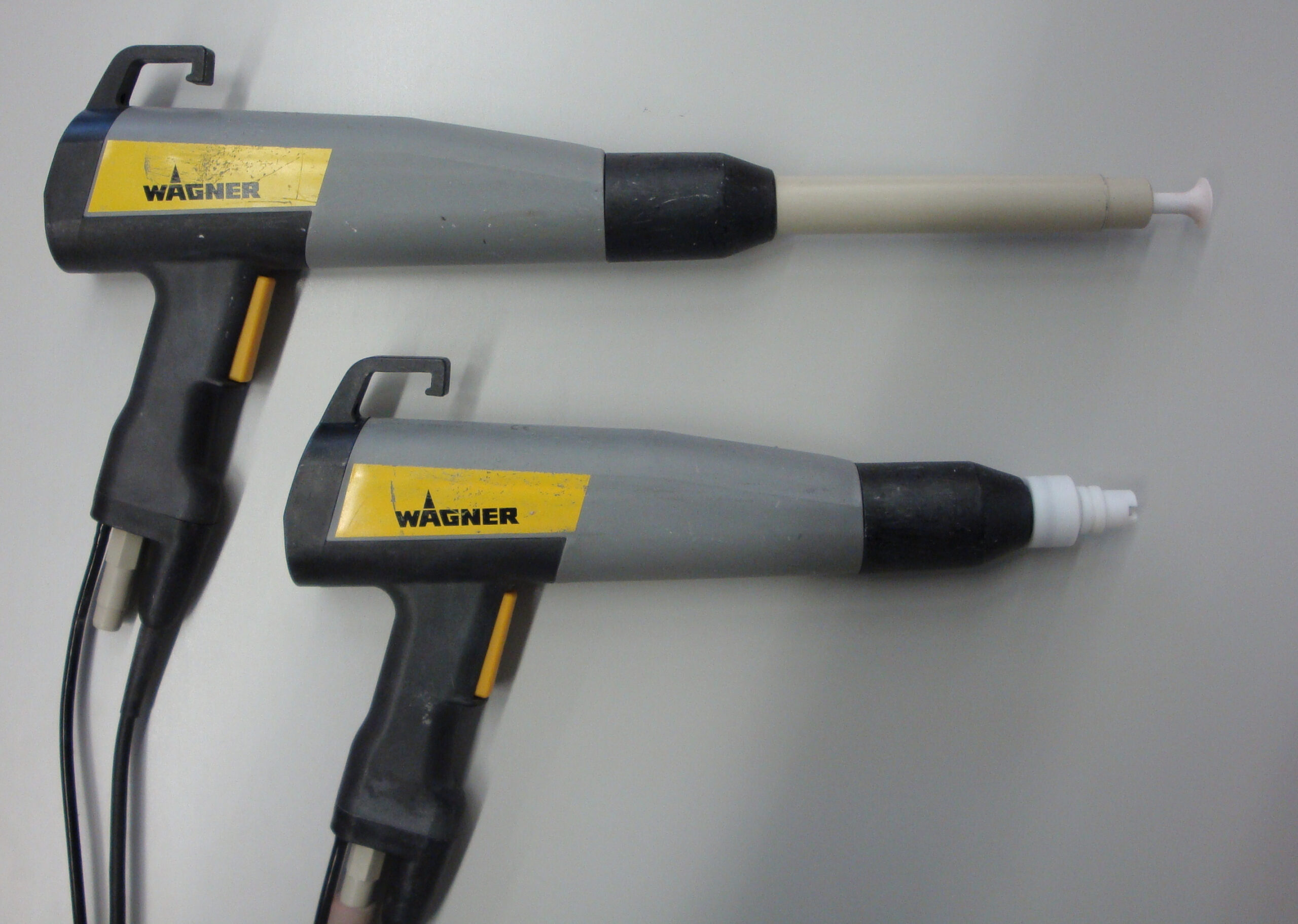 Comparison of two powder spray guns with visible nozzles and connected hoses