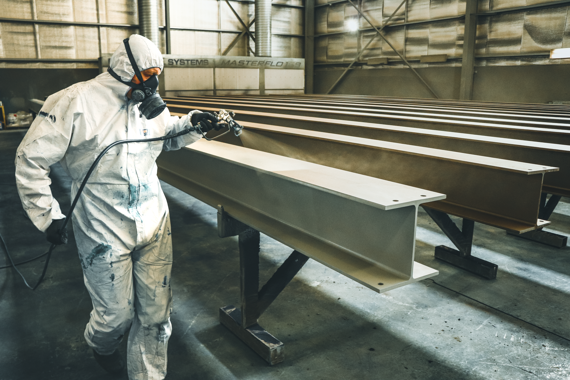 Worker in protective equipment spray finishing metal beams