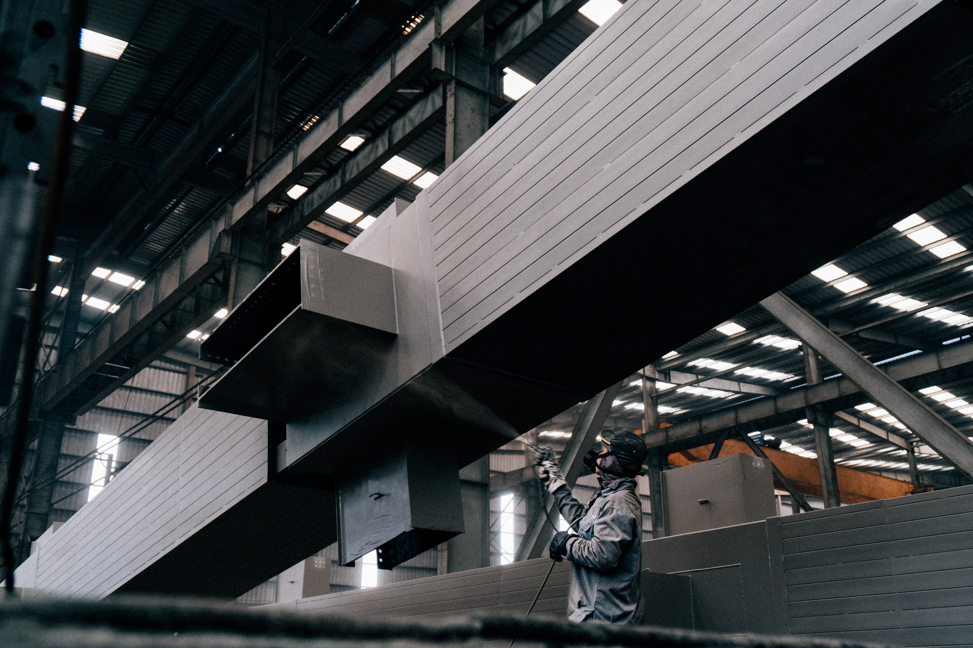 Worker spray finishing a large metal structure in an industrial facility